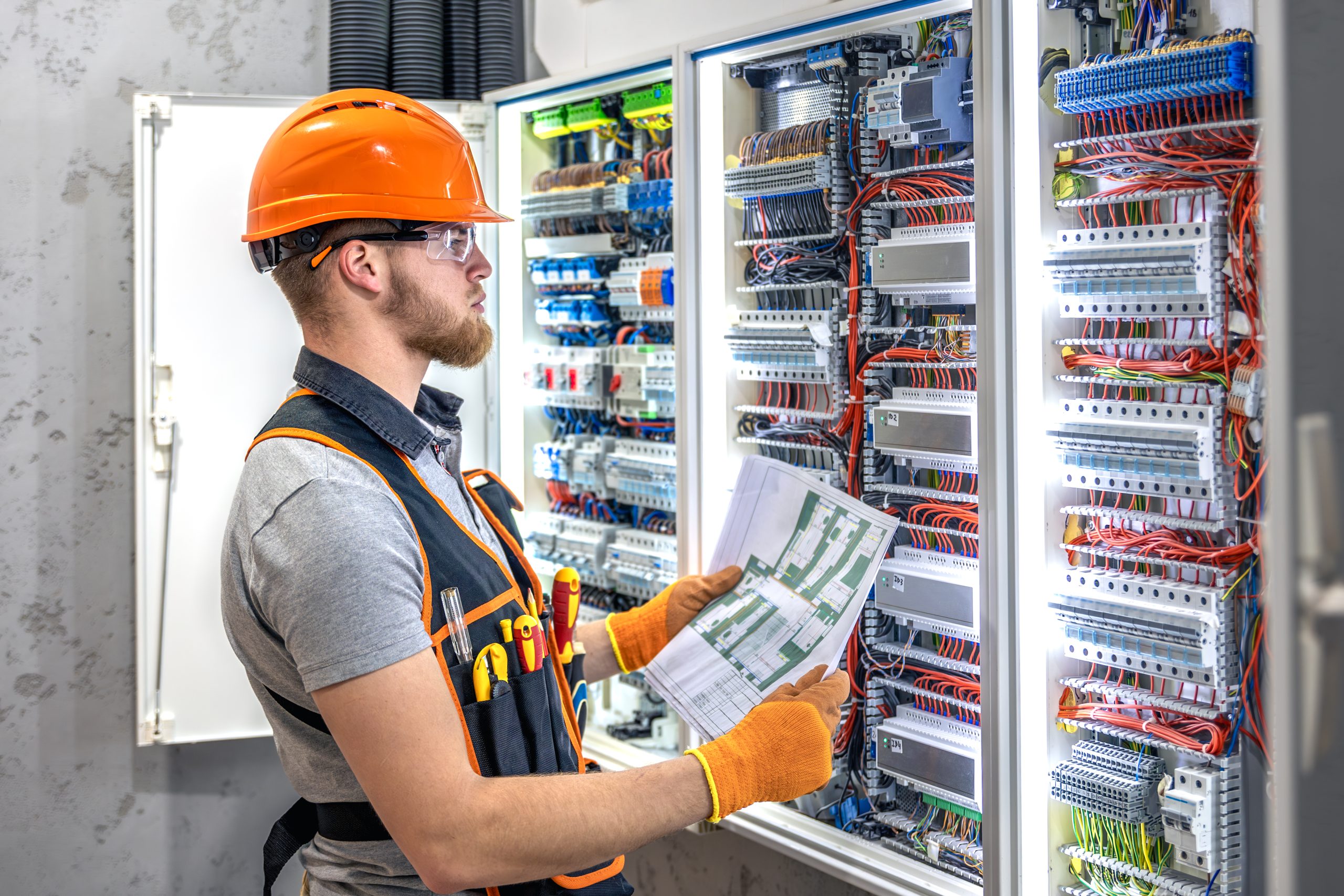 Male electrician working in electrical panel. Male electrician in uniform. High quality photo. Male construction worker in helmet and safety glasses.